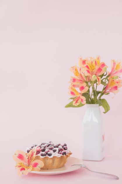 Tarta de arándanos con flor de alstroemeria sobre fondo rosa