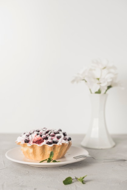 Tarta de arándanos en plato de cerámica blanca con florero