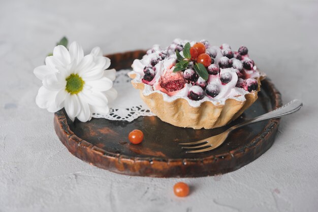 Tarta de bayas sabrosas con tenedor y flor en bandeja de madera redonda