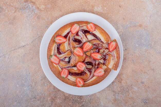 Tarta de fresa en un plato blanco con frutas alrededor.