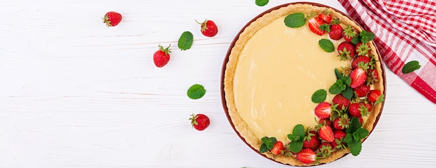 Tarta con fresas y crema batida decorada con hojas de menta en la mesa de luz. Vista superior