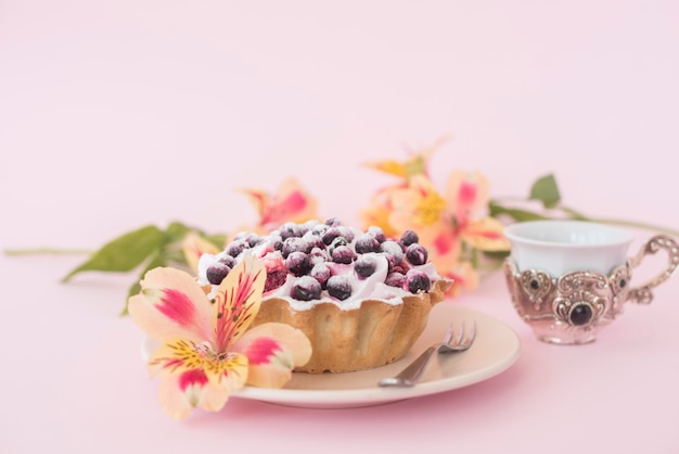 Tarta de frutas servida en un plato blanco con una flor de alstroemeria contra un fondo rosado