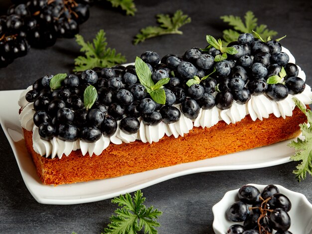 Tarta larga decorada con crema blanca y arándanos