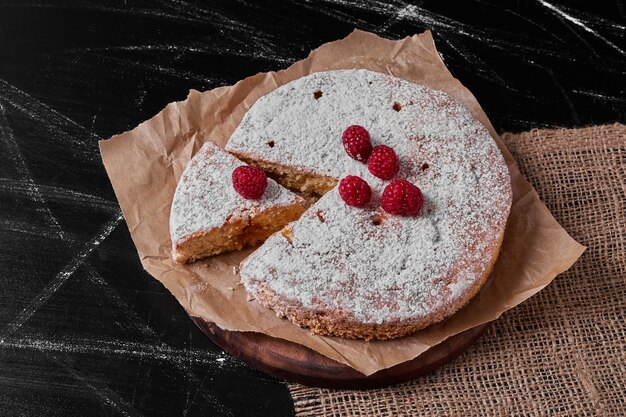 Tarta de limón con frutos rojos en bandeja de madera.