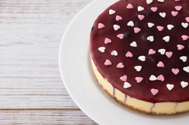 Tarta de queso con arándanos decorada con corazones dulces en una mesa de madera