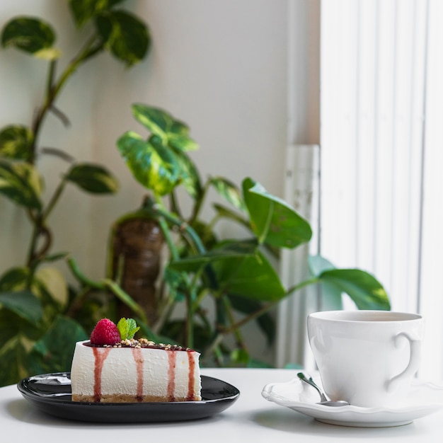 Foto gratuita tarta de queso con bayas; taza de café en la mesa en la cafetería cerca de la planta