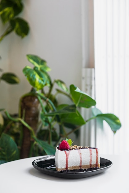 Tarta de queso dulce con bayas frescas en un plato de cerámica negro sobre la mesa blanca