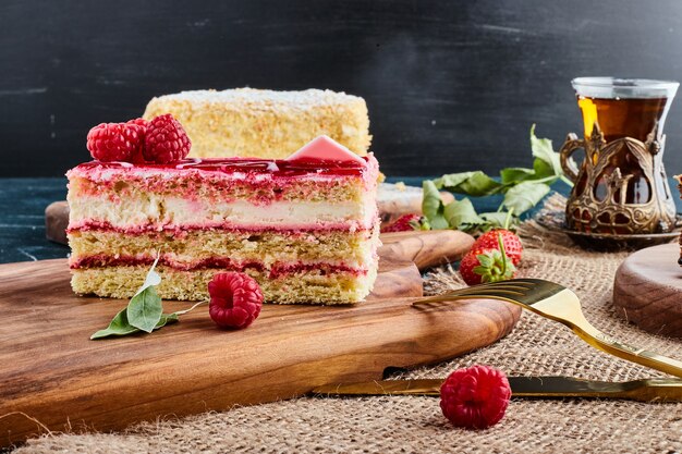 Tarta de queso de fresa con un vaso de té sobre una tabla de madera.