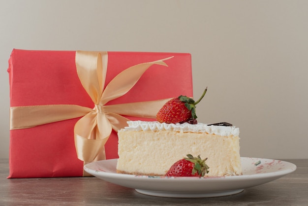 Tarta de queso con fresas y un regalo en mesa de mármol.