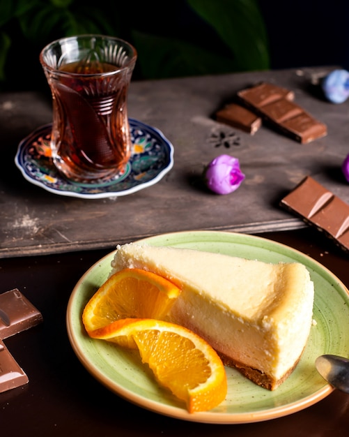 Tarta de queso servido con rodaja de naranja y vaso de té