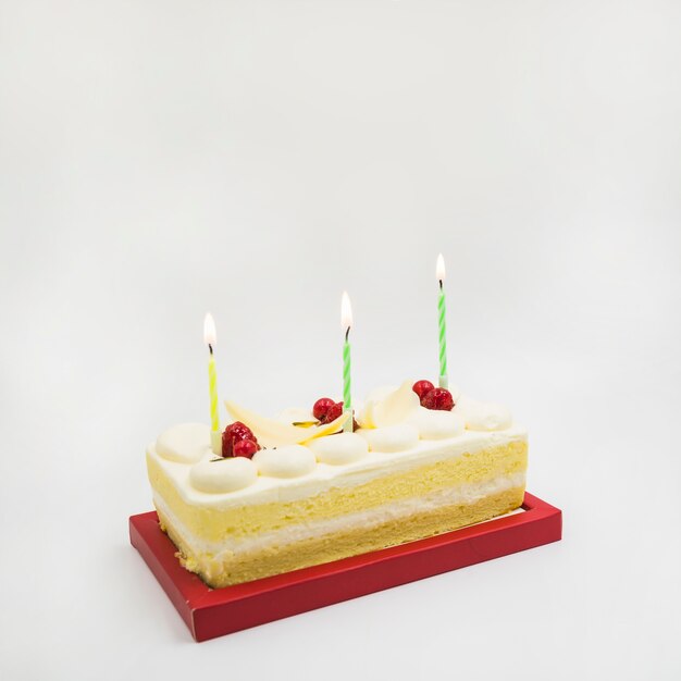 Tarta rectangular con velas encendidas sobre fondo blanco