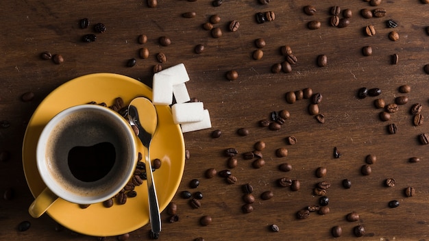 Foto gratuita taza amarilla con bloques de placa y azúcar cerca de los granos de café