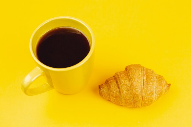 Taza amarilla con café y croissant sobre un fondo amarillo