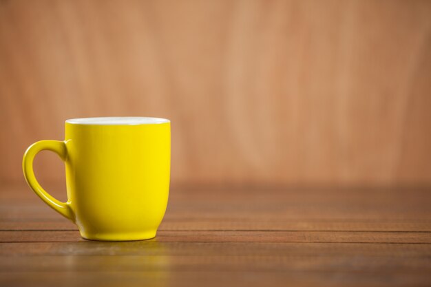 Taza amarilla de café en la mesa de madera