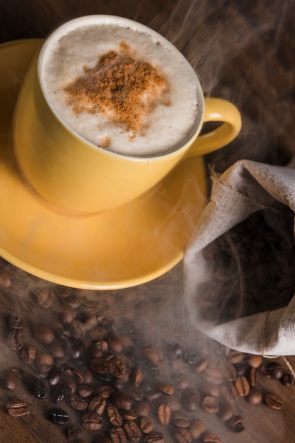 Taza con bebida caliente y granos de café esparcidos del saco.