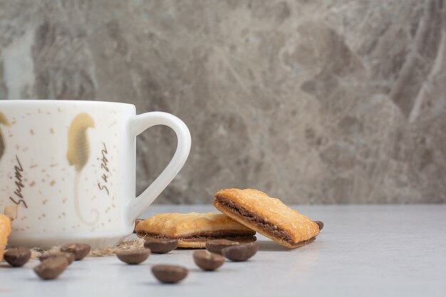 Taza blanca de café con galletas y granos de café sobre fondo blanco. Foto de alta calidad