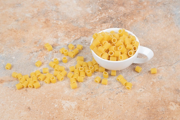 Foto gratuita una taza blanca llena de macarrones frescos sin preparar en el espacio de mármol.