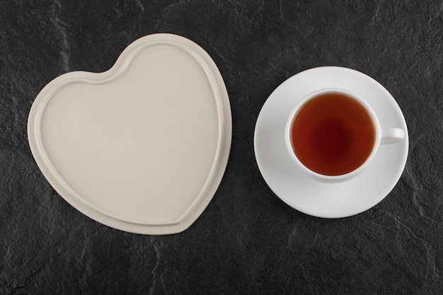 Una taza blanca de té caliente con un plato vacío.