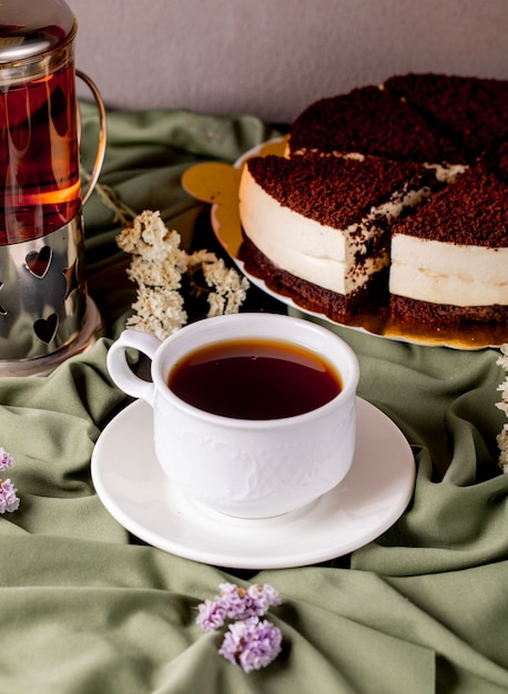 Una taza blanca de té y tetera con pastel de chocolate oreo.