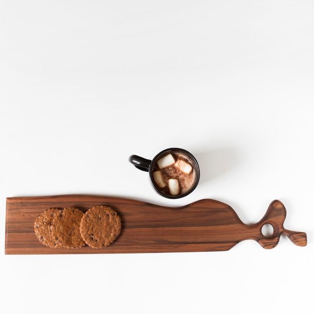 Taza de cacao junto a tabla de cortar decorativa con galletas.
