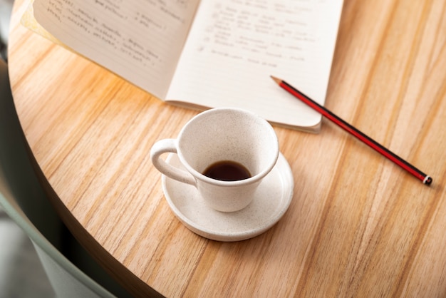 Taza de café de alto ángulo y cuaderno en la mesa