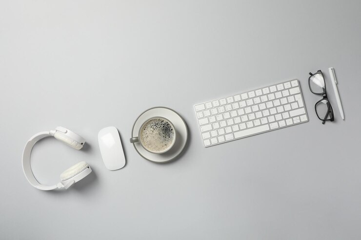 Foto gratuito una taza de café con auriculares y un teclado en un fondo claro