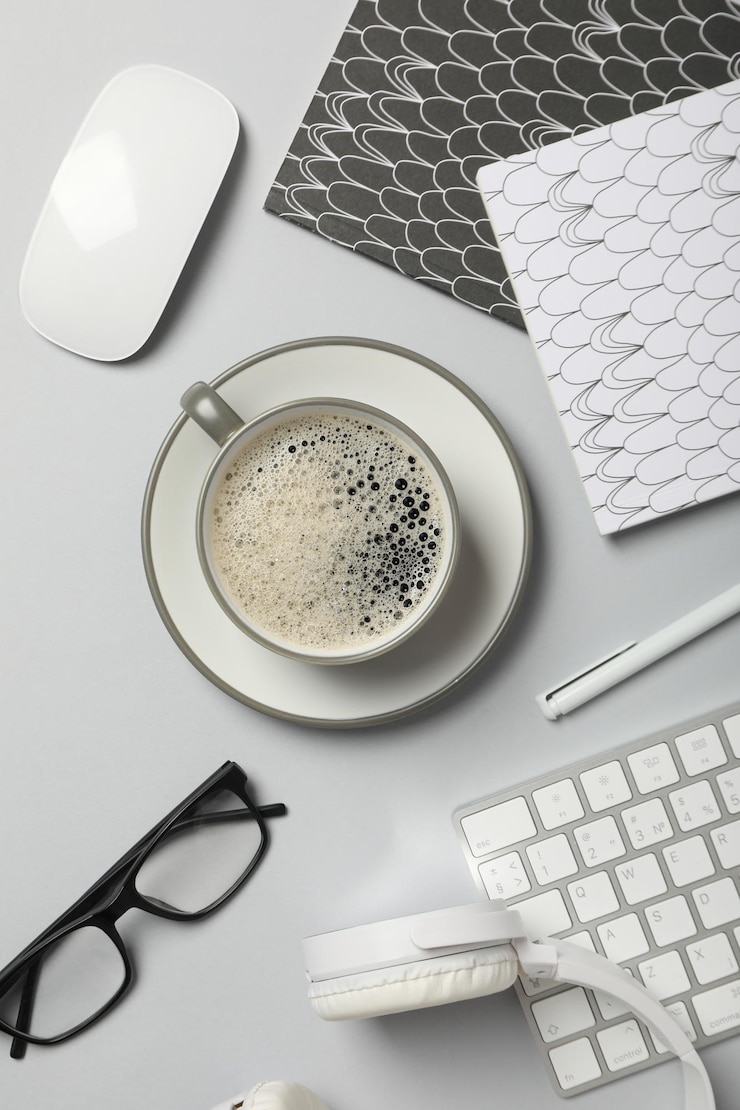 Foto gratuito una taza de café con auriculares y un teclado en un fondo claro