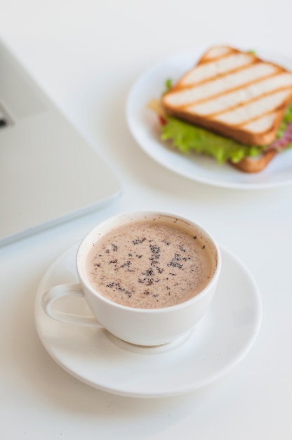 Taza de café blanca con sandwich sobre fondo blanco