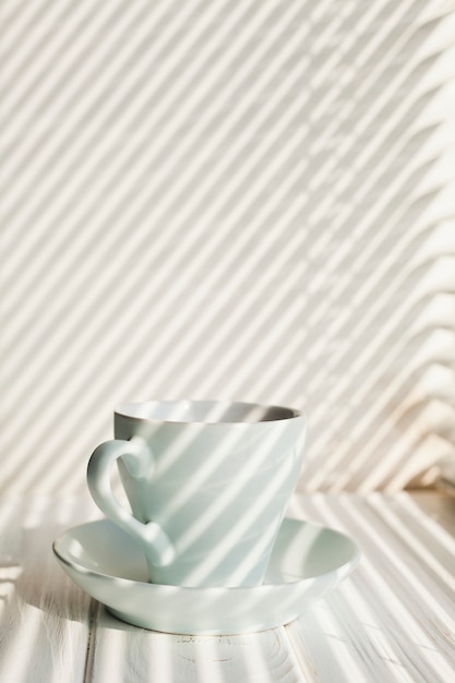 Taza de café blanco de cerámica con platillo cerca de la mesa de madera