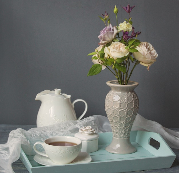 Una taza de café blanco, tetera y jarrón de flores.