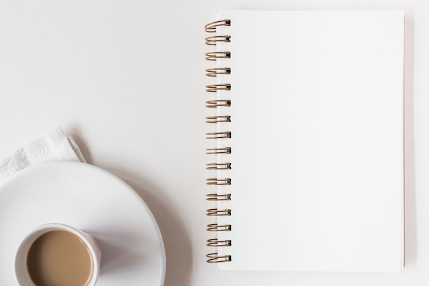 Taza de café y Bloc de notas espiral en blanco sobre fondo blanco