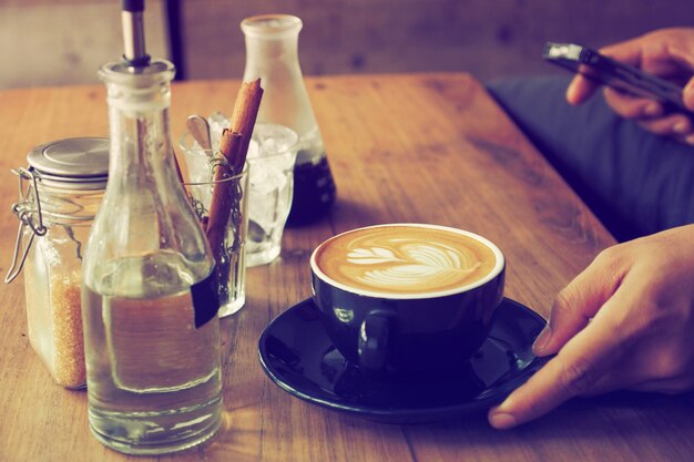 Taza de café con una botella de agua y un vaso con palos de canela sobre una mesa de madera