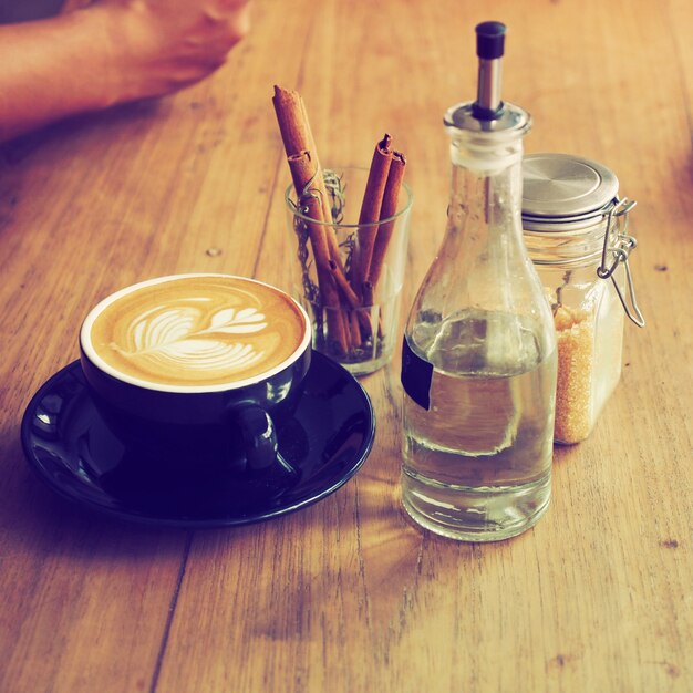 Taza de café con una botella de agua y un vaso con palos de canela