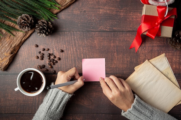 Taza de café y caja de regalo junto a la mano de la mujer está escribiendo la tarjeta de felicitación