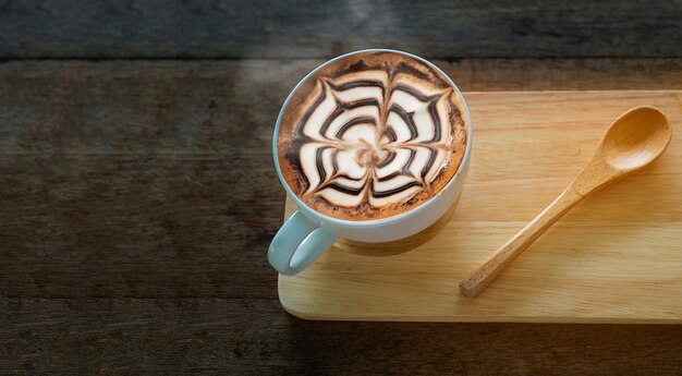 Taza de café caliente con una bonita decoración de arte Latte en una vieja mesa de textura de madera
