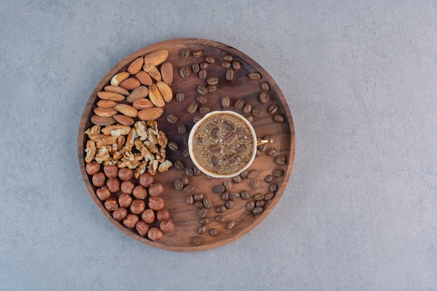 Taza de café caliente espumoso y diversas nueces en placa de madera.