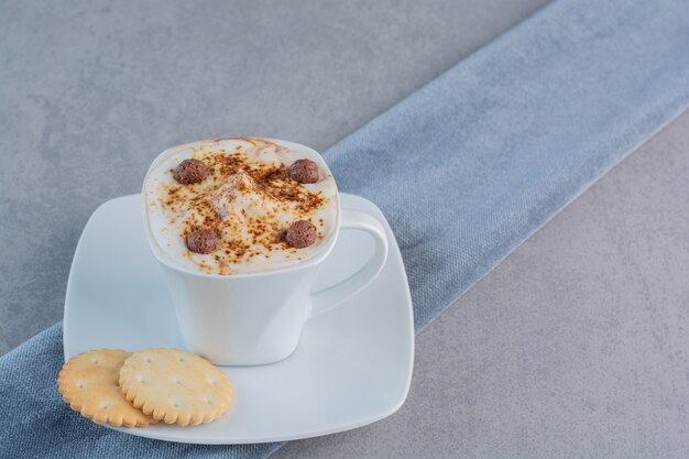 Taza de café caliente espumoso y galletas en piedra.