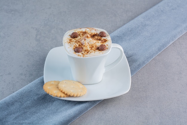 Taza de café caliente espumoso y galletas sobre fondo de piedra.