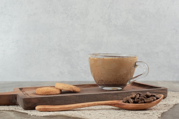 Taza de café caliente, galletas en tablero de madera con granos de café.