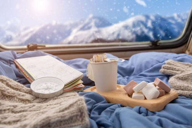 Una taza de café caliente con malvavisco cerca de la ventana con vistas a la montaña nevada