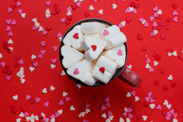 taza de café caliente con malvaviscos en forma de corazón y confetis en rojo