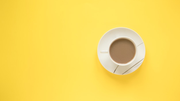 Una taza de un café caliente con platillo sobre fondo amarillo brillante