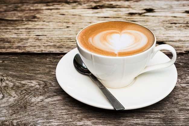 Taza de café caliente vintage con una bonita decoración de arte Latte en una vieja mesa de textura de madera