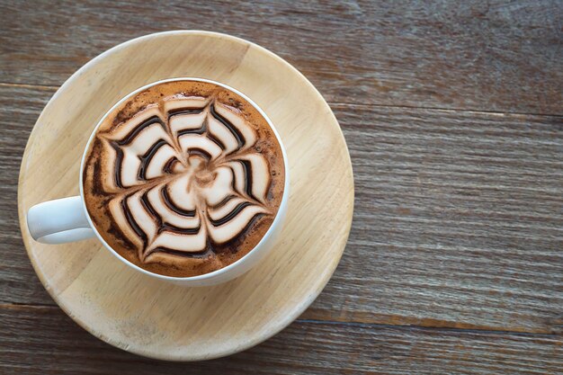 Taza de café caliente vintage con una bonita decoración de arte Latte en una vieja mesa de textura de madera