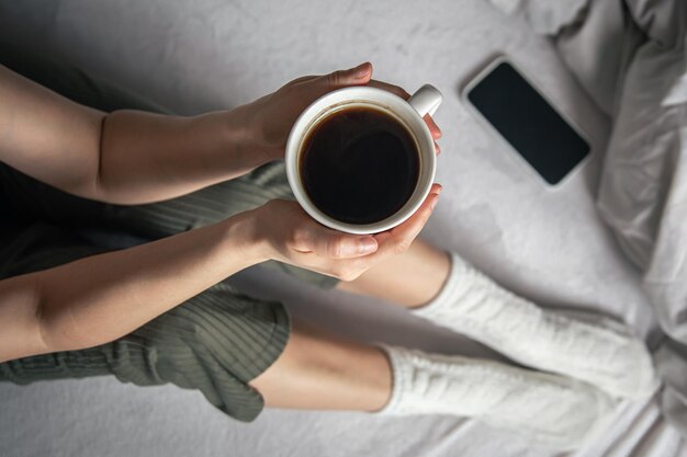 Taza de café en la cama en manos femeninas vista superior