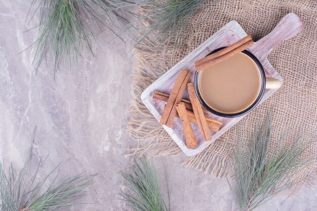 Una taza de café con canela en rama sobre tabla de madera rústica.