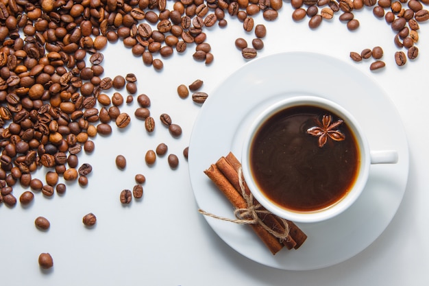 Una taza de café con canela seca vista superior con granos de café en la superficie