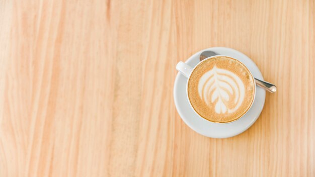 Taza de café capuchino con latte de arte y cuchara sobre fondo de madera