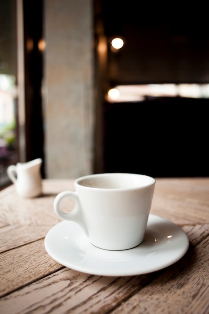 Foto gratuita taza de café de cerámica blanca con platillo en mesa de madera