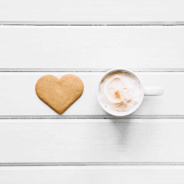 Foto gratuita taza de café cerca de una galleta en forma de corazón